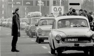 A west German border policeman stands aside as a stream of East Germans arrive in the west