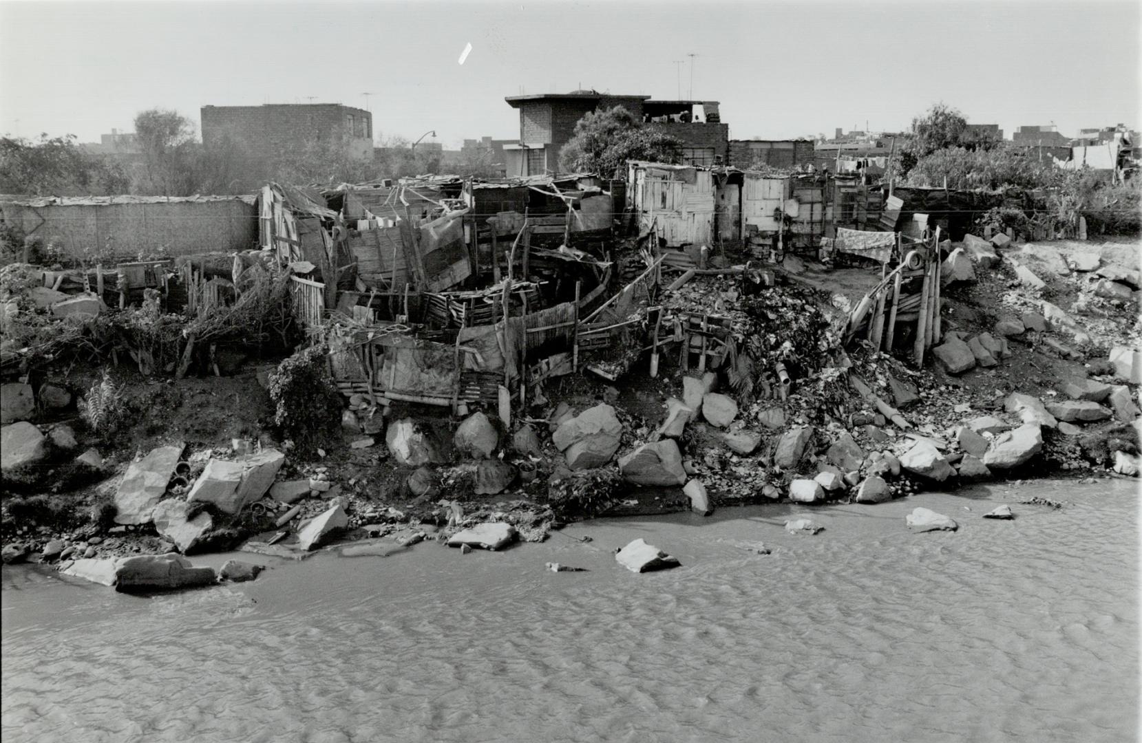 Small huts stand on the banks of the polluted Rio Rimac, Lims's main river