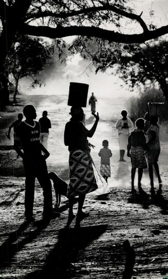 Silhouetted against the sun, villagers gather around the well