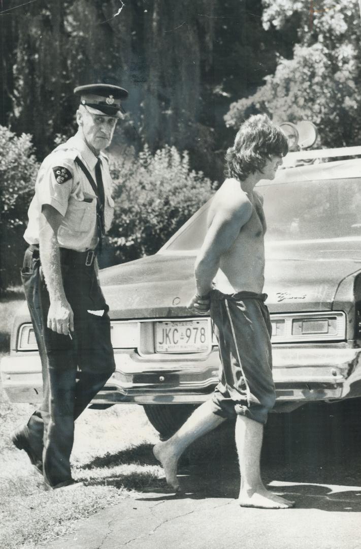 Handcuffed suspect is led to OPP cruiser yesterday after manhunt in area north of intersection of Highways 7 and 27