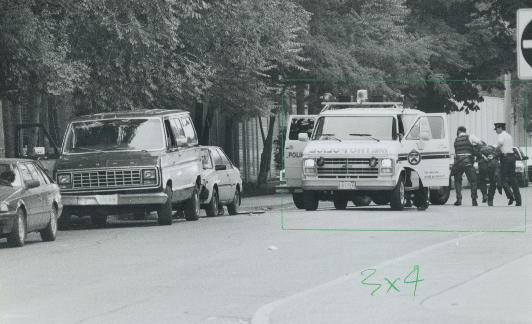 Double check: A police officer uses a mirror on a stick to check the interior of a van while another covers him after a suspect, below, who was sleeping in the van is bundled into a paddy wagon