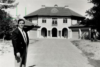 Image shows a real estate agent standing in front of a two storey residential house.