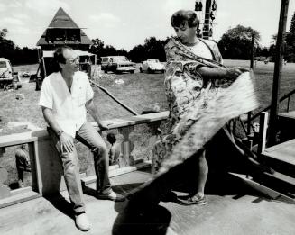 An actor swirls the robe of a costume, while a man in casual clothes looks on.