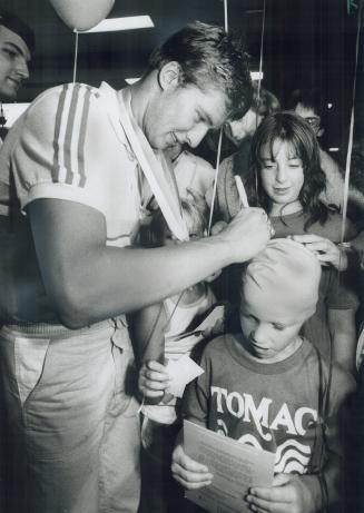 Home as a hero: Alex Baumann was greeted by mob of admirers at Pearson International Airport yesterday, including Ryan Slaney of Mississauga, who had swim hat autographaed