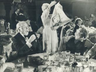 Pierre Berton and wife et, howl with laughter as sister Lucy Woodward shows a boyhood photo at dinner in his honor