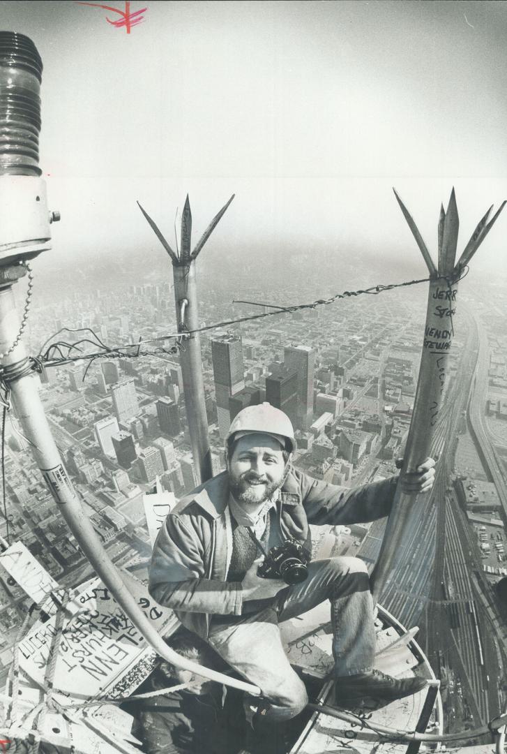 Image shows a photographer at the top of the CN Tower with an aerial view of Toronto in the bac…