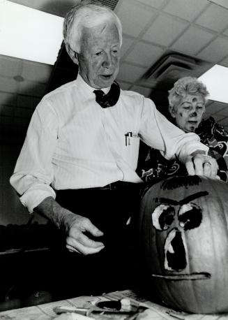 Put on a scary face. City of York Mayor Fergy Brown rolls up his sleeves and tries his hand at carving a jack-o'-lantern for the United Way yesterday. Clown Ev Viney looks on