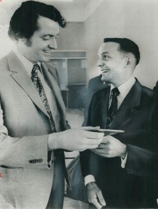 Laughing heartily with Leslie James (left) of Canada's External Affairs department, Quebecker Marc Cayer prepares to board a plane at Saigon for his j(...)