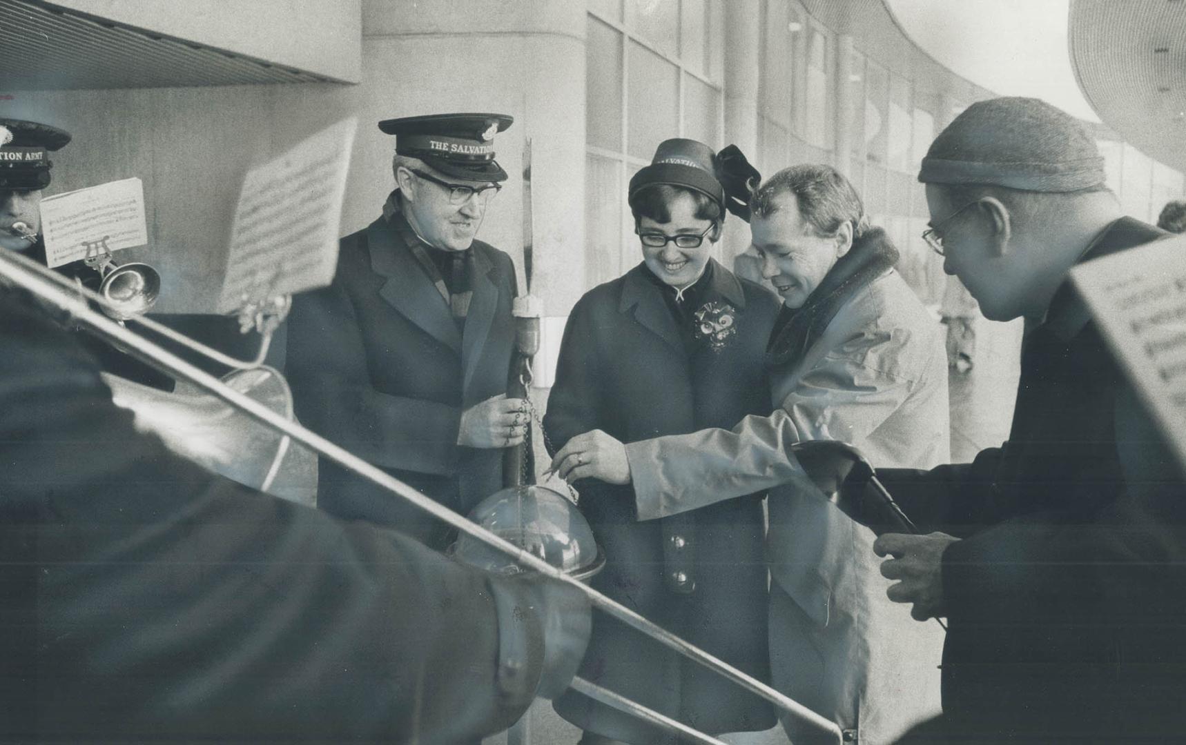 Christmas Kettle at city hall. Accompanied by Brigadier Ted Dyck and Betty Ann Lewis, mayor elect David Crombie slips the first donation into Salvatio(...)