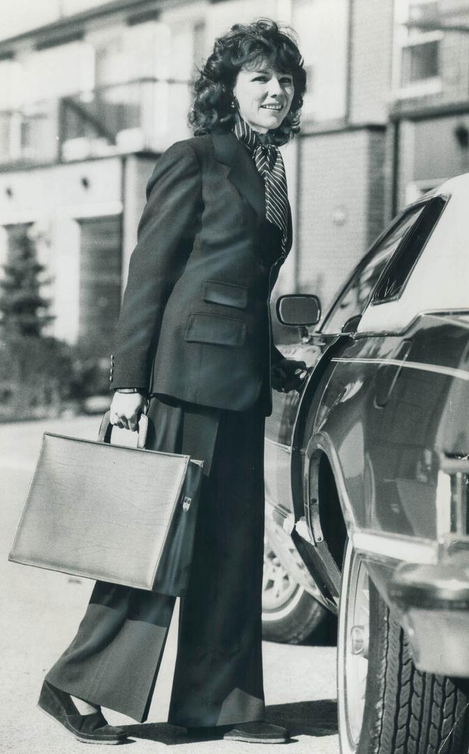 Faye Dance, co-host on Wintario, wears navy pants, Ralph Lauren navy blazer, pin-striped blouse and carries briefcase