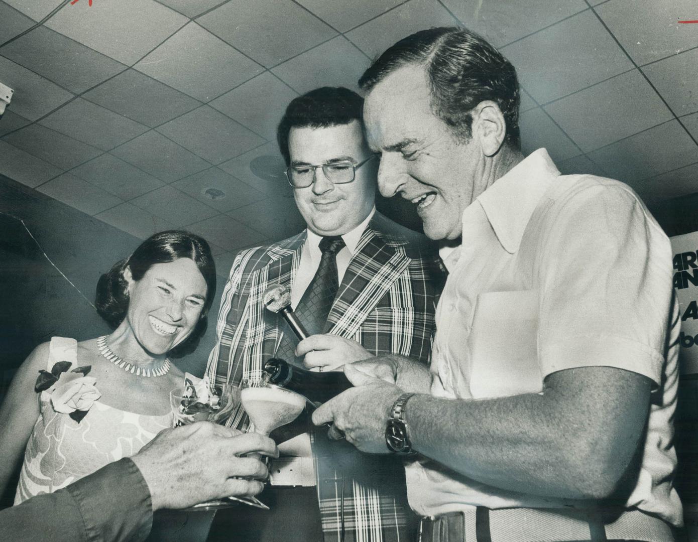 Pouring a toast, Barney Danson, the Liberal who defeated uranium millionaire Stephen Roman in York North riding, stands on the victory platform with h(...)