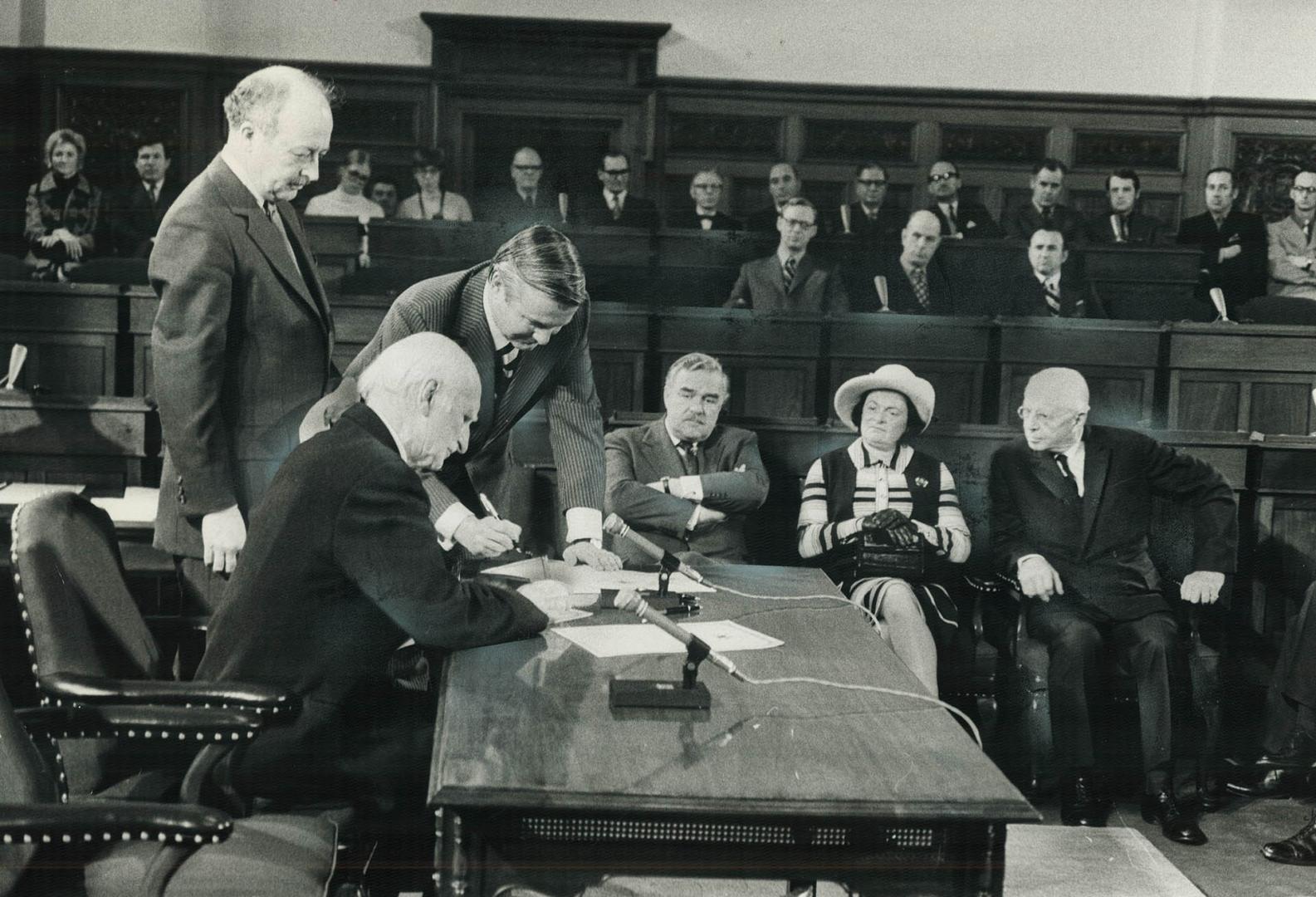 Formally taking power as premier of Ontario, William Davis stands at corner of table in the legislative chamber at Queen's Park as Lieutenant-Governor(...)