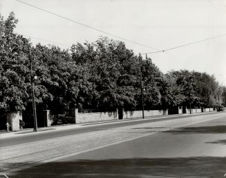 View of long, low brick wall, left, running parallel to adjacent sidewalk and empty stretch of …