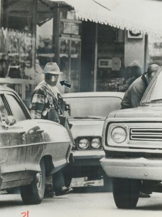 A Bank Robber in stocking mask, holding a deadman's detonator in his teeth (arrow), walks from a Kenora bank behind a policeman stowing money in a tru(...)