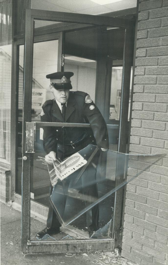 Hold-up scene: A policeman removes broken glass from a door police smashed to get into a bank during a robbery attempt in North York yesterday