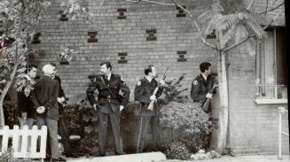 Armed Metro policemen peer round the corner of a Wellesley Street apartment building after armed man fired several shots