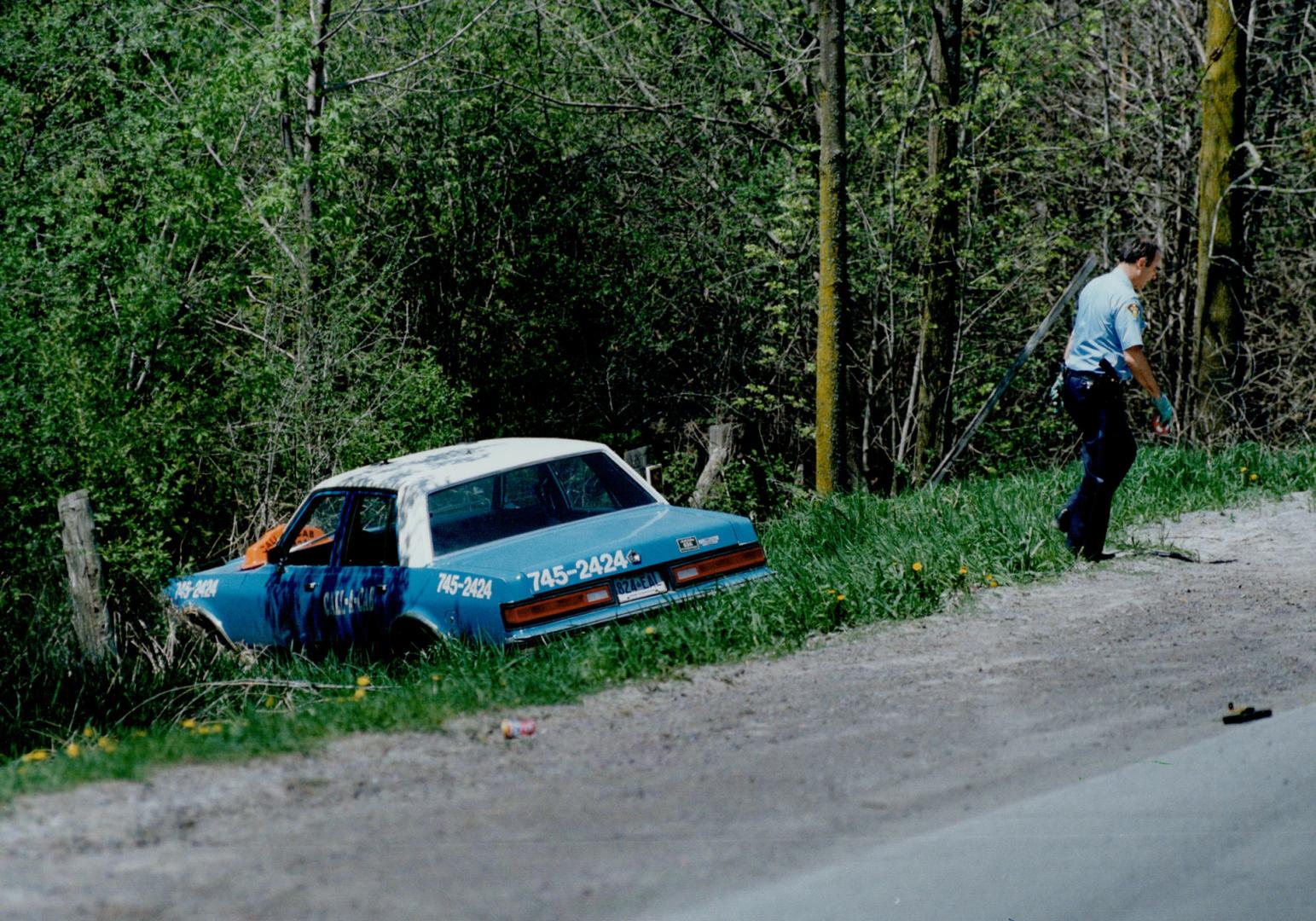 Grisly end: An Ontario Provincial Police officer walks from the commandeered taxt in which a man killed himself yesterday with a 12-gauge shotgun after wounding two officers near Peterborough