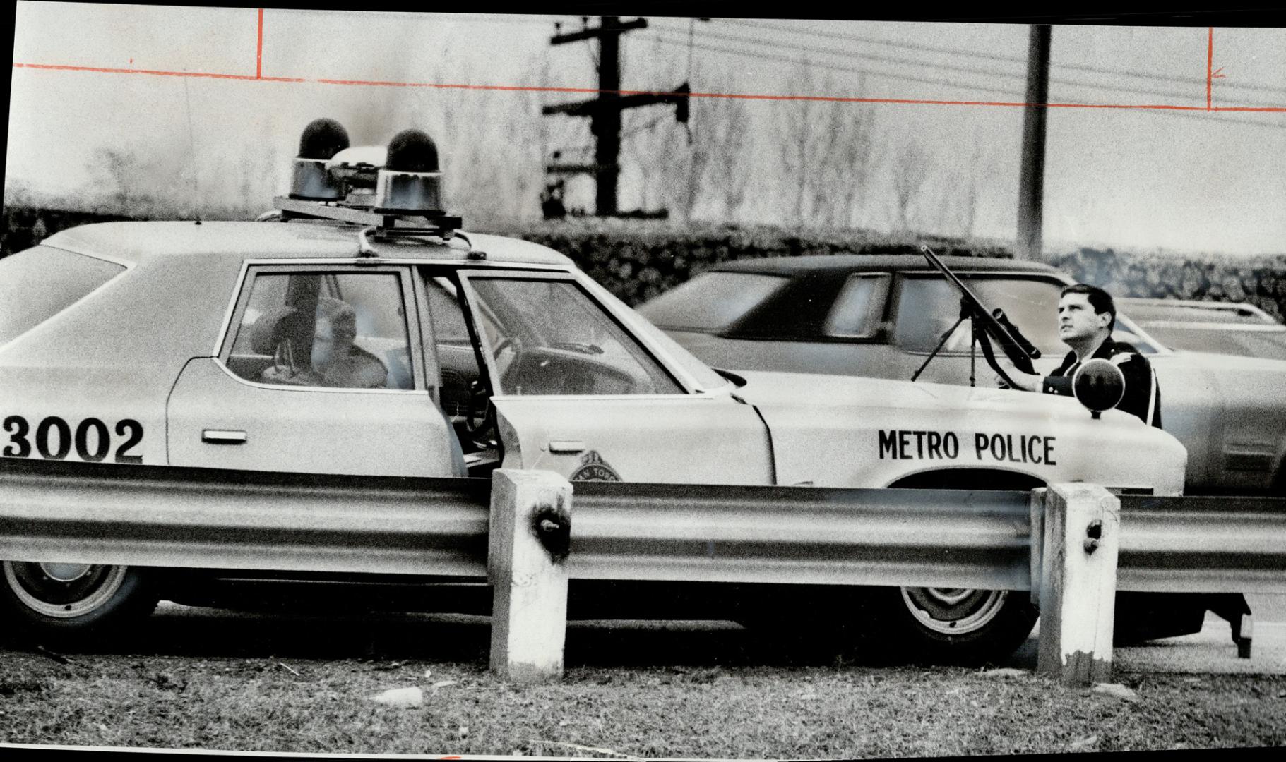 Watching a building from which a sniper fired on the Don Valley Parkway yesterday, a police officer crouches behind his car, a telescopic sight on his(...)