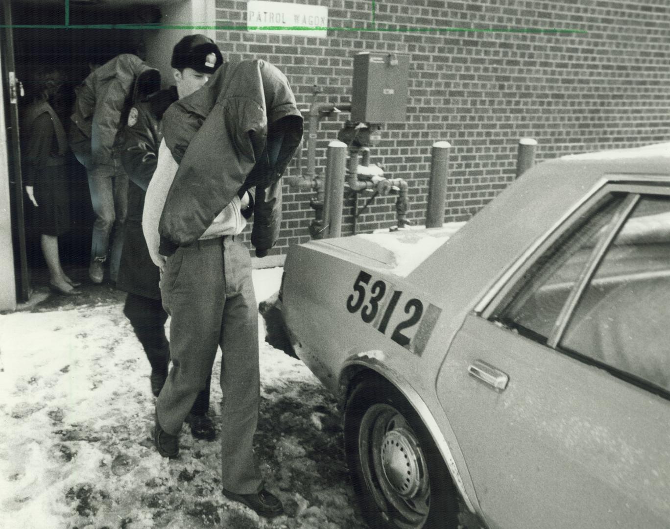 Held in slaying: Two suspects, charged with first-degree murder in the slaying of 16-year-old Gary Brown, cover their faces from news photographers as they are led to a police car