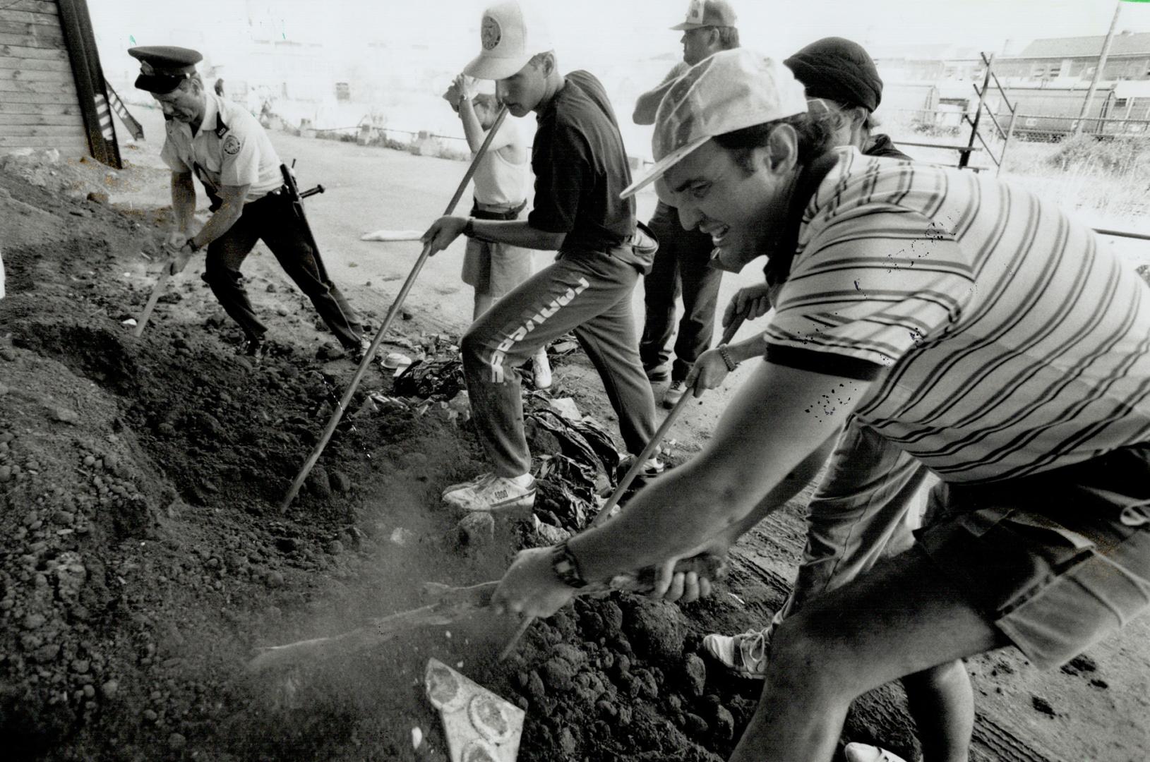 Grim task: A police officer, left, joins people searching in a pile of dirt at the Canadian National Exhibition grounds yesterday for missing girl