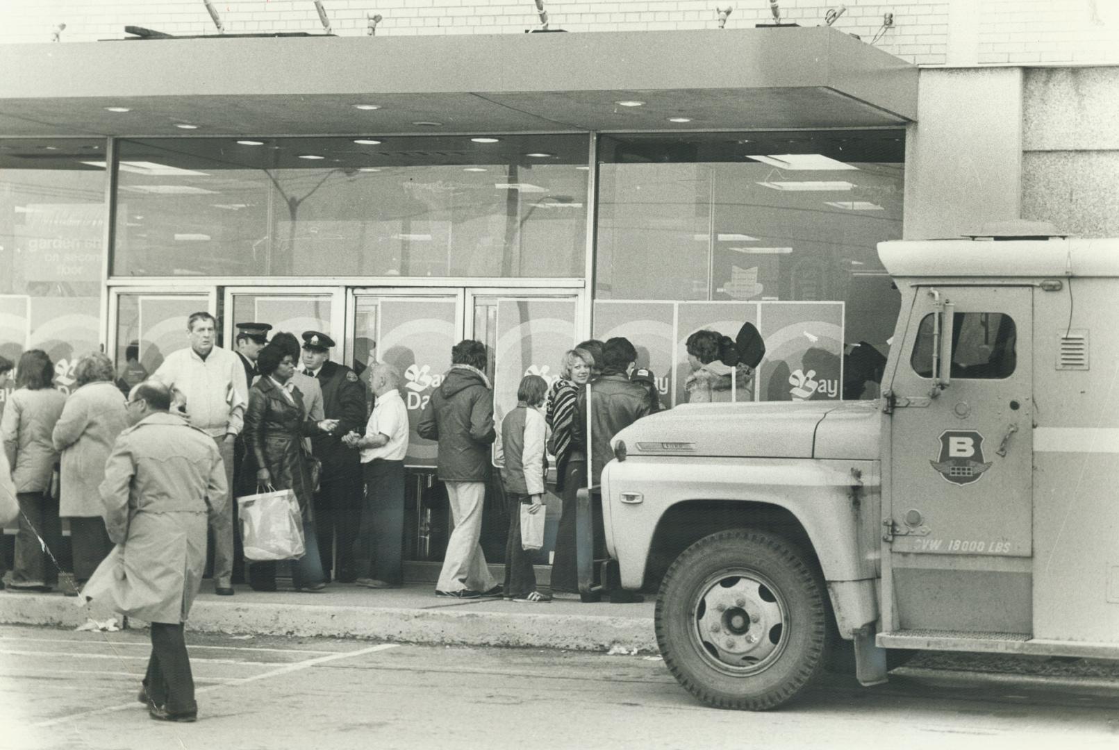 Bystanders mill about entrance moments after a store employee was killed and a Brink's messenger wounded and robbed of $50,000 yesterday in a Scarboro(...)