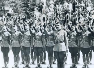 Two rows of RCMP officers doff their hats in their right hands and cheer. In the background, sp…