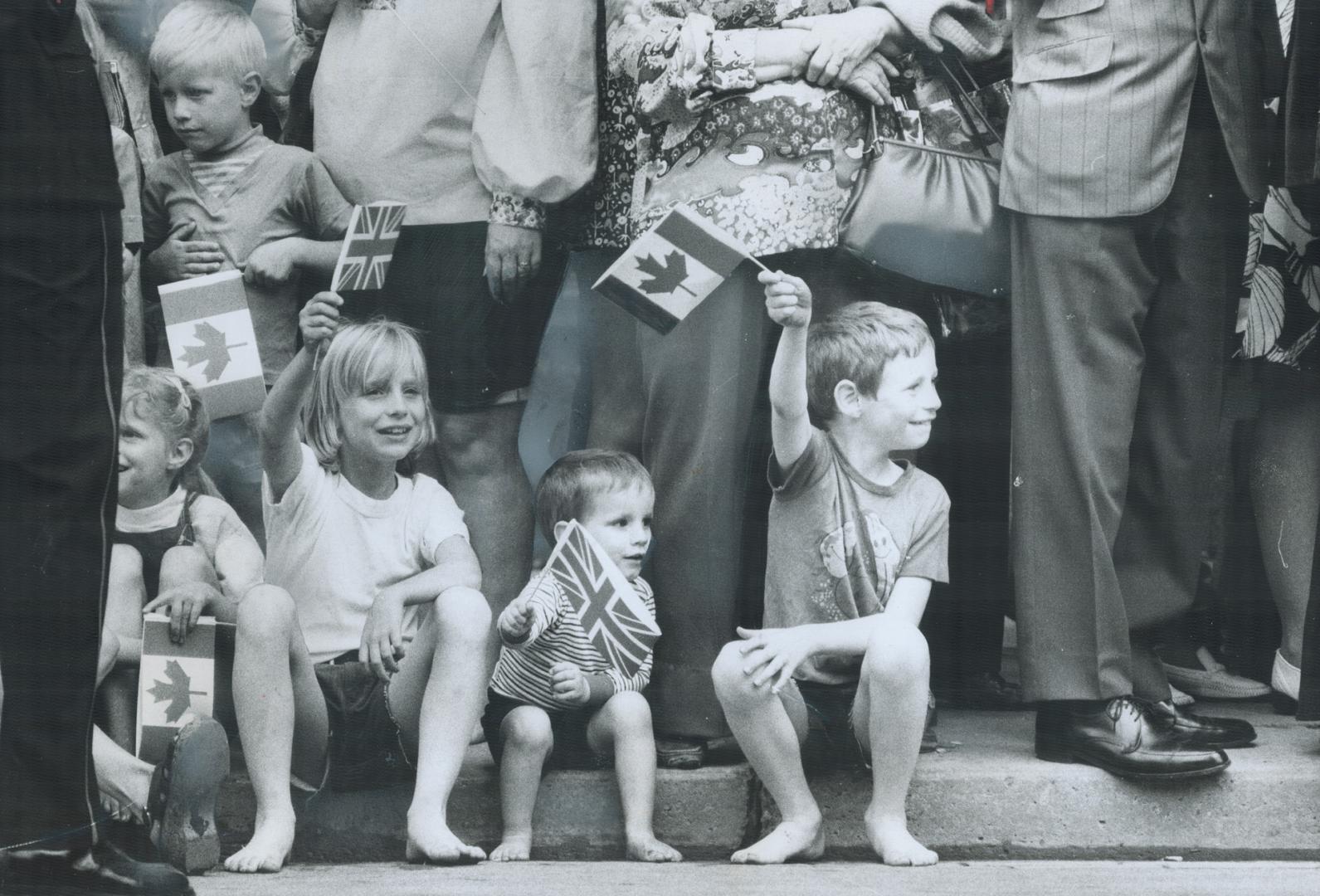 Young fans of the Queen sit on the curb near the Royal York Hotel, waving canadian flags and Union Jacks as she left, in the Ontario landau, for Queen(...)