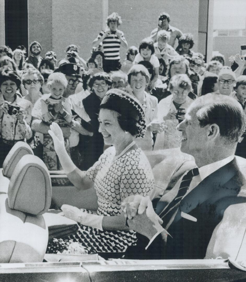 The Queen, accompanied by Prince Philip, waves to the smiling crowd lining the streets of St