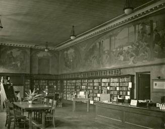 Image shows an interior of the library branch with a desk on the right, book stacks along the w…