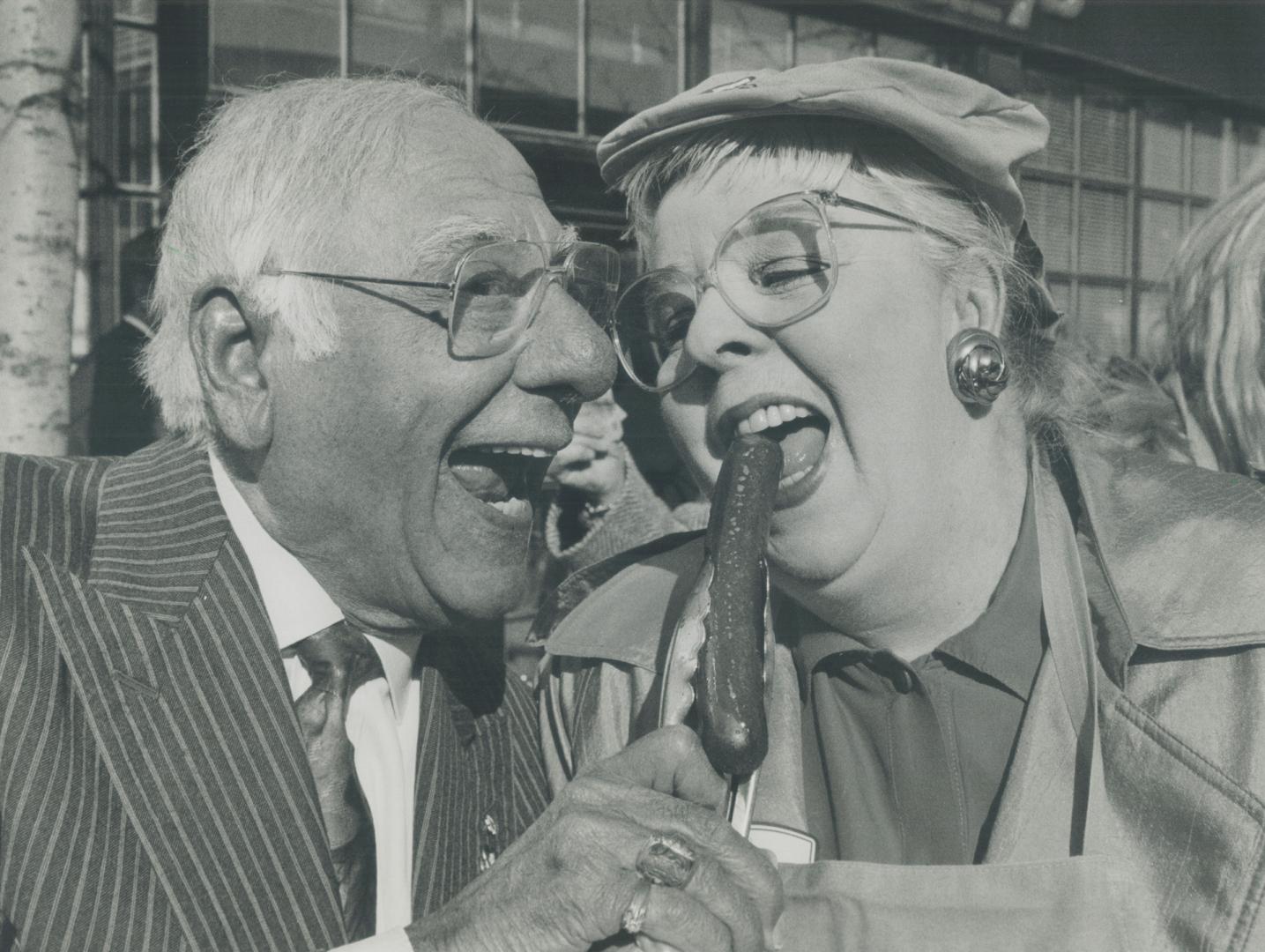 Johnny Lombardi, president of CHN radio, and actress Barbara Hamilton dig in to a dog yesterday at Shopsy's celebrity outdoor barbecue in front of Sho(...)