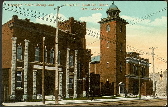 Two red-brick, two-storey buildings with towers. The road is unpaved, with streetcar tracks. Te…