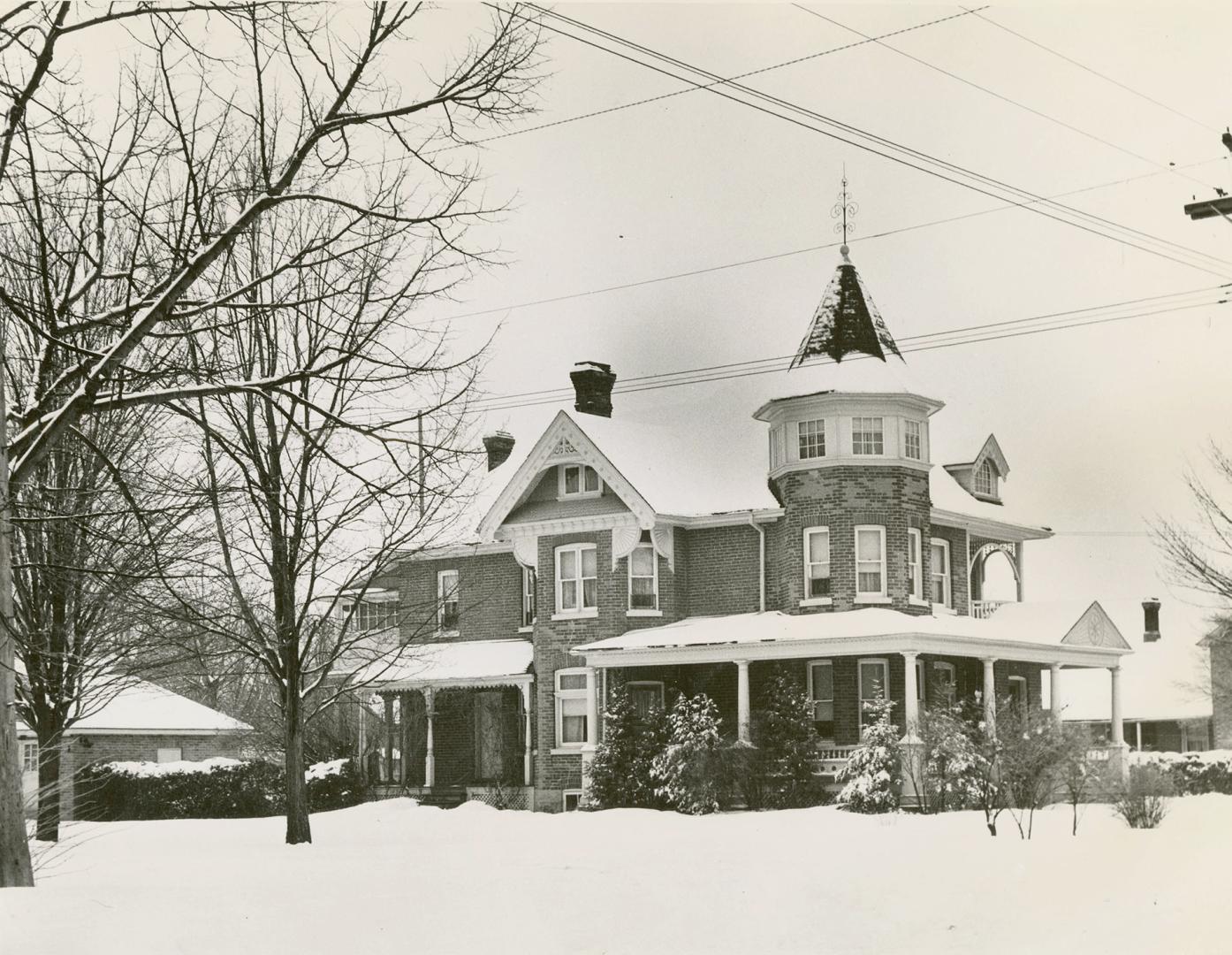 Shows a large stone house with a turret, gingerbread eaves and dormer windows. A wrap-around po…