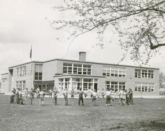 Two-storey, light brick building with flat roof, large windows and flagpole attached, left. Lar ...