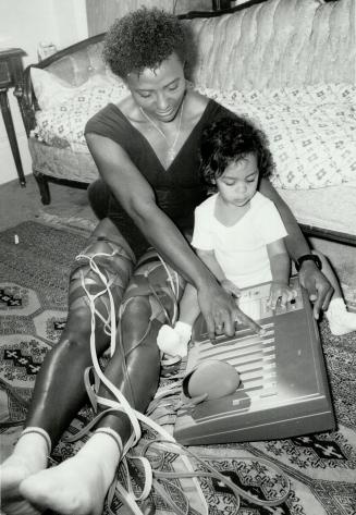 Home workout: Angella Issajenko looks after her daughter, Sacha, while strengthening her legs with electronic muscle stimulator