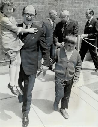 A new home for 24 children, Ontario Minister of Social and Family Services John Yaremko carries Robin, 8, as he walks with Ronnie, 8, to cut ribbon to(...)