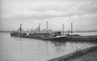 Image shows a tugboat docked at the island with the Toronto Harbour in the background.