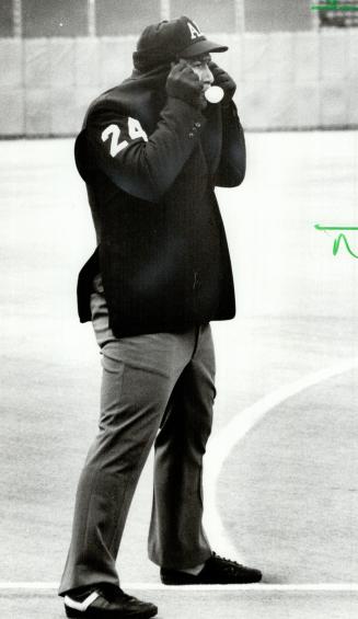 The summer game? Third base umpire Al Clark shields himself from th gusting winds that once again plagued the Jays-Rangers games. He passes time blowing bubbles while warming his ears