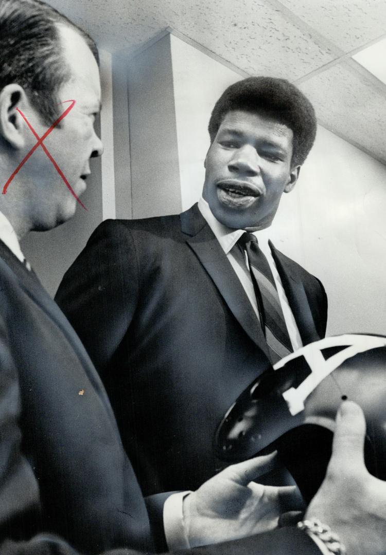 Veron Vanoy (right), a 6-8, 270-pounder from University of Kansas, checks an Argonaut football helmet with coach Leo Cahill after his singing was anno(...)