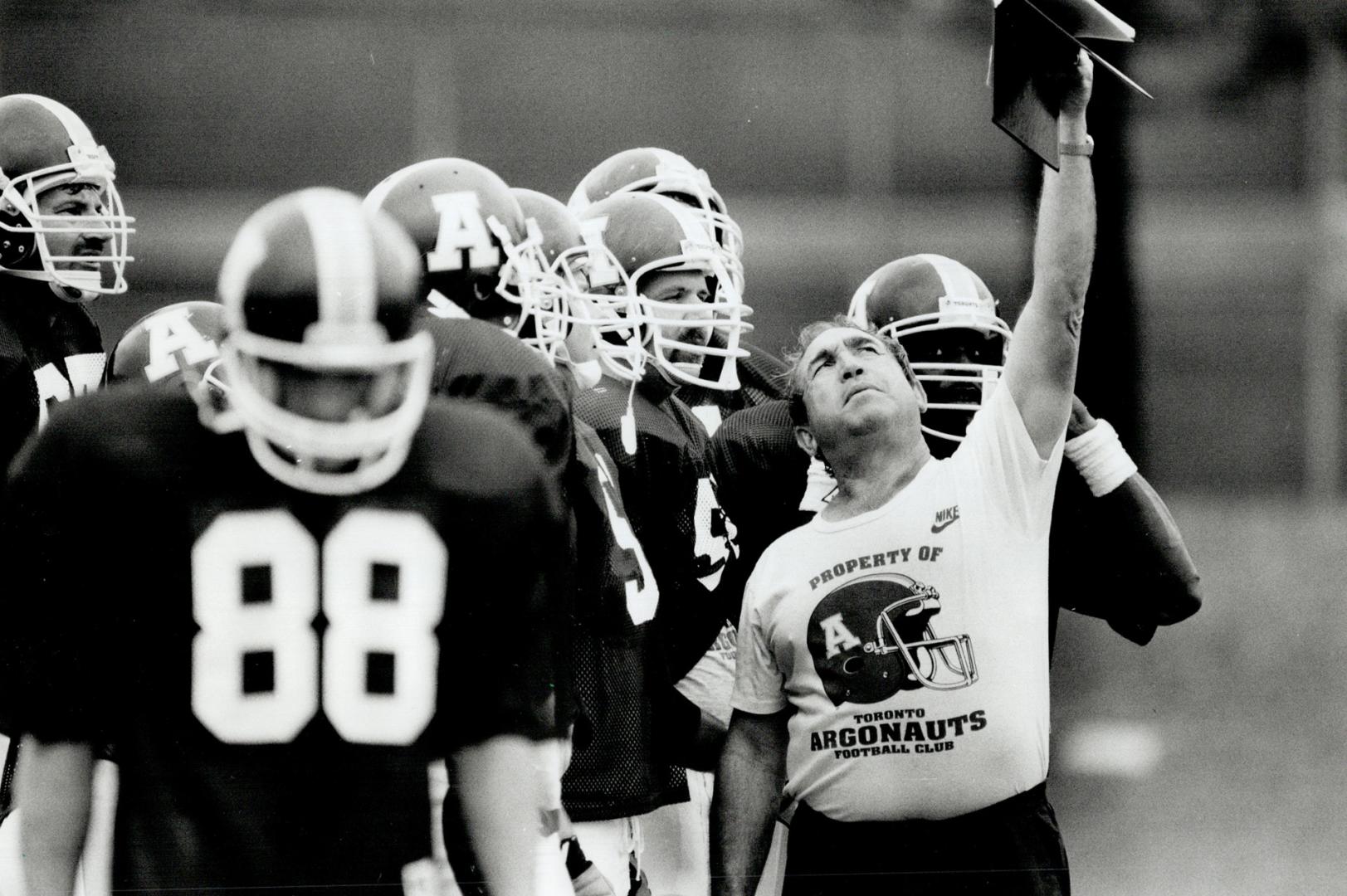 See, dick? Run! Dick, Run! Toronto Argonauts offensive line coach John Payne holds up the team's precious playbook for the benefit of his attentive troops during a scrimmage yesterday