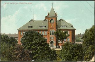 Trees in the foreground, and in the background, a two story high school building, with a tower …