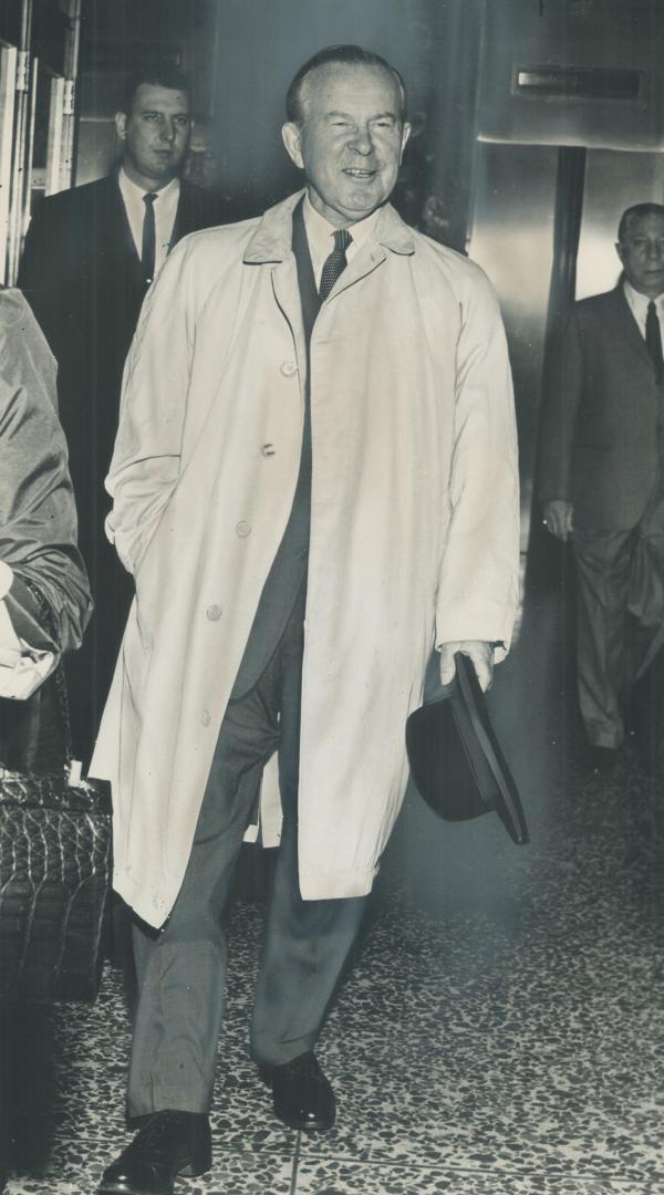 Election smile? Prime Minister Pearson, dressed for the rains that soon came, is shown leaving the Park Plaza hotel for a luncheon engagement in Toronto today