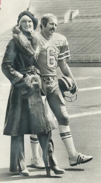 Model walking with Mike Rae is wearing a mahogany colored leather coat with wide belt and raccoon collar