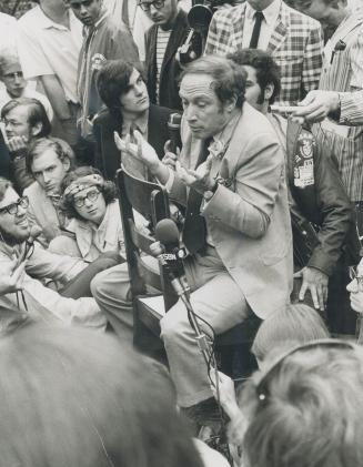 Prime Minister Pierre Trudeau sits astride a wooden chair while talking to a group of young people in the back yard of the Guelph Youth Hotel today as(...)