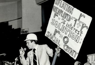 Banner-waving: With hard hat on head and banner in hand, John Turmel, the independent Social Credit candidate in the Spadina by-election, makes a point during an all-candidates meeting Monday