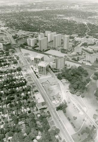 Aerial view of several clusters of tall buildings right of multi-lane roadway; overhead view of…