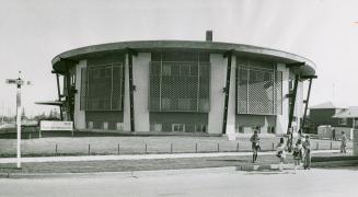 Octagonal, disc shaped, three-storey flat-roofed building with large mesh panels covering secon…