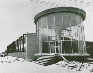 Six steps lead to transparent, circular enclosure attached to low brick building seen in rear.  ...