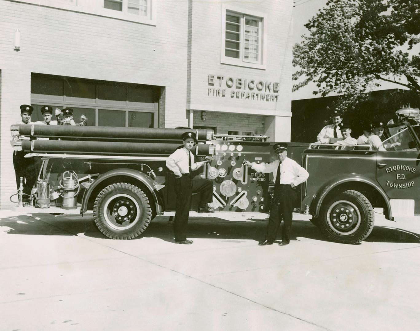 Men in dark, peaked service caps, white shirts, dark pants and ties- pose with fire truck in fr…