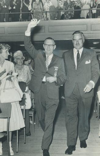 Arm in arm with Premier John Robarts, Kenneth Waters, conservative candidate, enters hall