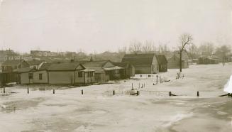 Row of one and two-storey houses in close proximity to each other, surrounded by icy flood wate…